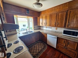 Kitchen featuring extensive wood cabinetry, a double basin stainless steel sink, a tile countertop, a tile backsplash, and wood-finish flooring - 