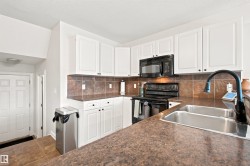Kitchen featuring white cabinetry with dark hardware, a dual basin stainless steel sink with a dark faucet, a black electric range, and a black microwave - 
