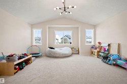 Spacious bonus room featuring vaulted ceilings, neutral carpeting, and a modern chandelier - 