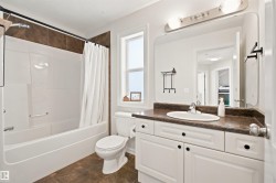 Bathroom featuring a single window, white bathtub with a tiled surround, a toilet, a vanity with a dark countertop, and a large wall-mounted mirror - 