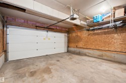Spacious garage featuring a white sectional overhead door, automatic opener, concrete flooring, and built-in overhead shelving for storage - 