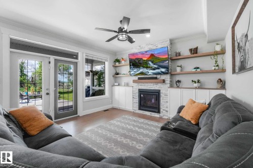Living area featuring a white stone-clad natural gas  fireplace with a wood mantle, built-in shelving, and wood-finish flooring - 553006 Range Road 153, Rural Two Hills County, AB - Indoor Photo Showing Living Room With Fireplace