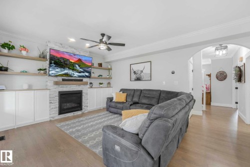 Living area featuring a stone-clad natural gas fireplace with wood mantel, built-in cabinetry, floating shelves, and light wood-finish flooring - 553006 Range Road 153, Rural Two Hills County, AB - Indoor Photo Showing Living Room With Fireplace