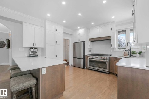 Gourmet kitchen featuring a built-in stainless steel range, custom range hood, recessed lighting, wood-finish flooring, and a breakfast bar with stone countertops - 553006 Range Road 153, Rural Two Hills County, AB - Indoor Photo Showing Kitchen With Upgraded Kitchen