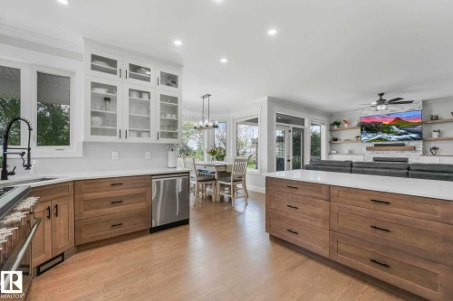 Open-concept living area with wood-finish flooring, a kitchen island with storage, white upper cabinetry with glass fronts, integrated stainless steel appliances, and a dining area with a chandelier - 553006 Range Road 153, Rural Two Hills County, AB - Indoor Photo Showing Kitchen