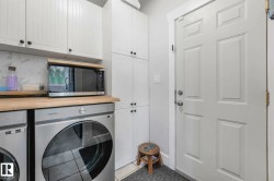 Laundry area featuring white shaker-style cabinetry, wood-finish countertops, stainless steel appliances, and a paneled door - 