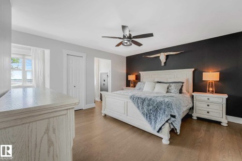 Spacious bedroom featuring light wood-finish flooring, a ceiling fan with integrated lighting, a contrasting accent wall, and a wide window with natural light - 553006 Range Road 153, Rural Two Hills County, AB - Indoor Photo Showing Bedroom