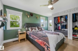 Bedroom featuring wood-finish flooring, a ceiling fan with integrated lighting, and two windows with white trim - 