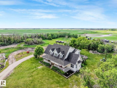 Expansive property featuring a residence with a covered porch, multiple dormer windows, and a dark shingle roof, set within a verdant landscape - 553006 Range Road 153, Rural Two Hills County, AB - Outdoor With View