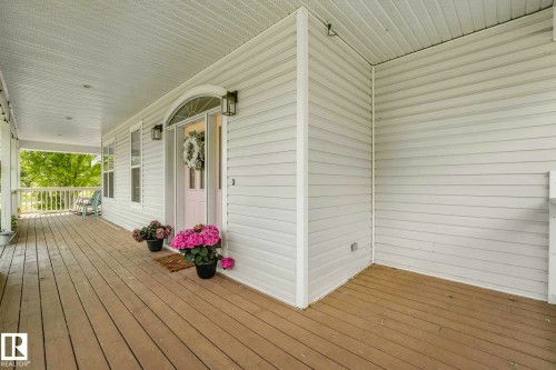 Spacious front covered porch with wood-finish flooring, white siding, and a white arched entry door - 553006 Range Road 153, Rural Two Hills County, AB - Outdoor With Deck Patio Veranda With Exterior