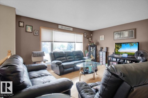 Living room featuring wood-finish flooring and a large window with privacy blinds - 5506 53St, Mundare, AB 
