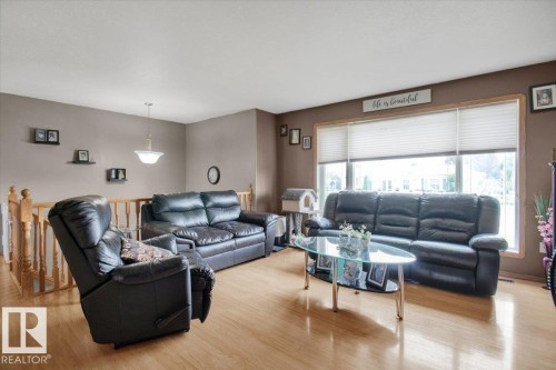 Spacious living area featuring wood-finish flooring, a large window with horizontal blinds, and a staircase with wood railing - 5506 53St, Mundare, AB 