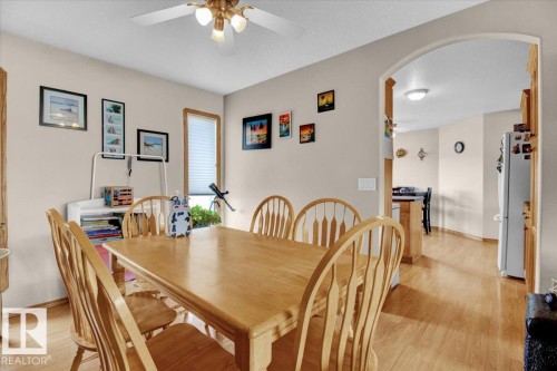 Dining area featuring wood-finish flooring, a ceiling fan with integrated lighting, and an arched doorway opening to a kitchen area - 5506 53St, Mundare, AB 