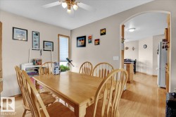 Dining area featuring wood-finish flooring, a ceiling fan with integrated lighting, and an arched doorway opening to a kitchen area - 