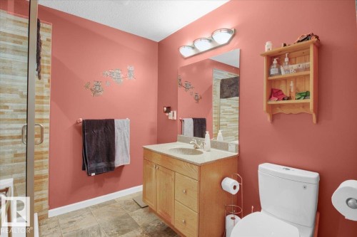 Bathroom featuring a glass-enclosed shower with horizontal tile detailing, a wood-finish vanity with an integrated sink and countertop, a wall-mounted mirror, and a three-light vanity fixture - 5506 53St, Mundare, AB 