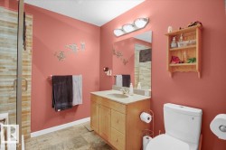 Bathroom featuring a glass-enclosed shower with horizontal tile detailing, a wood-finish vanity with an integrated sink and countertop, a wall-mounted mirror, and a three-light vanity fixture - 