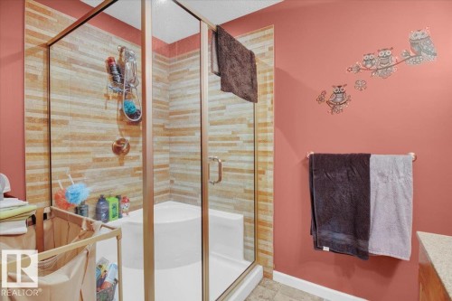 Shower enclosure with glass panels and a framed door, featuring a tiled interior with horizontal stone-finish accents - 5506 53St, Mundare, AB 