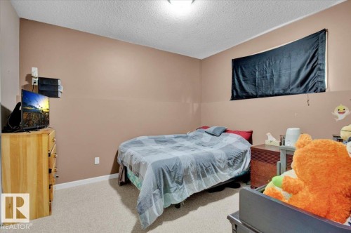 Carpeted bedroom with neutral-toned walls, a textured white ceiling, and a visible electrical outlet - 5506 53St, Mundare, AB 
