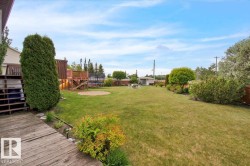 Expansive backyard featuring a lush lawn, a multi-level wooden deck structure, a circular sand pit, and mature perimeter landscaping - 