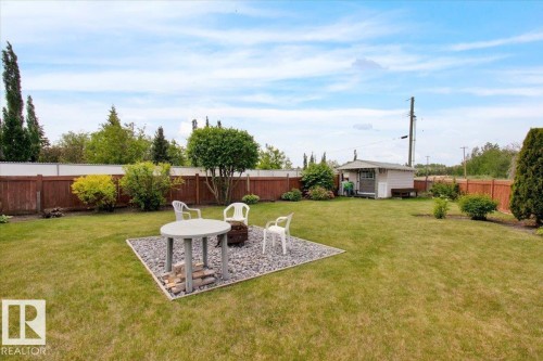 Expansive backyard featuring a large lawn, a dedicated gravel patio area, mature trees, and a wooden privacy fence - 5506 53St, Mundare, AB 