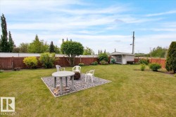 Expansive backyard featuring a large lawn, a dedicated gravel patio area, mature trees, and a wooden privacy fence - 