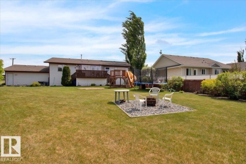 Expansive backyard featuring a manicured lawn, a gravel fire pit area, and mature trees - 5506 53St, Mundare, AB 