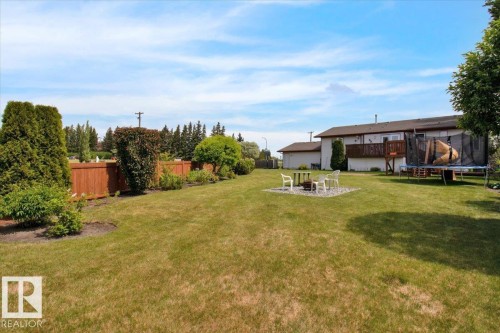 Spacious backyard featuring a wood privacy fence, established perimeter landscaping, a gravel fire pit area, and a rear wood deck - 5506 53St, Mundare, AB 