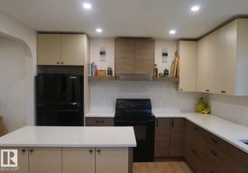 Contemporary kitchen featuring a center island with a light-toned countertop, a mix of light and dark wood-finish cabinetry, a white textured backsplash, and recessed ceiling lighting - 25 8930 99 Avenue, Fort Saskatchewan, AB 