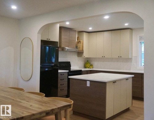 Kitchen featuring a central island with countertop, two-tone cabinetry, tiled backsplash, black appliances, and recessed lighting - 25 8930 99 Avenue, Fort Saskatchewan, AB 