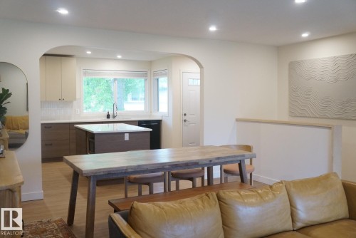 Open concept kitchen and dining area featuring an arched doorway, recessed lighting, wood-finish flooring, a kitchen island with seating, and a large window above the kitchen sink - 25 8930 99 Avenue, Fort Saskatchewan, AB 