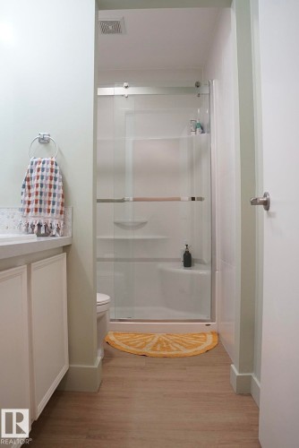 Bathroom featuring a glass-enclosed shower with a sliding door, white vanity cabinetry, light-toned wood-finish flooring, and a white toilet - 25 8930 99 Avenue, Fort Saskatchewan, AB 