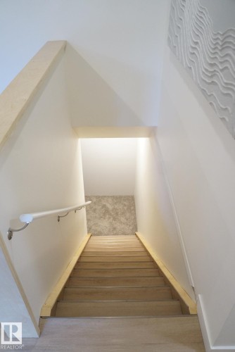Staircase featuring wood-finish treads, a contrasting wall-mounted handrail, and a textured accent wall at the landing - 25 8930 99 Avenue, Fort Saskatchewan, AB 