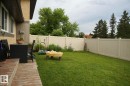Expansive backyard featuring a manicured lawn, a full-height privacy fence, and mature perimeter trees - 25 8930 99 Avenue, Fort Saskatchewan, AB 