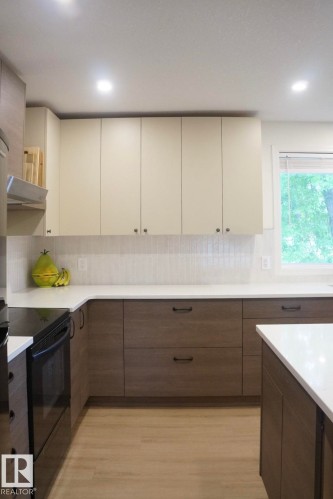 Modern kitchen featuring light upper cabinetry and wood-finish lower cabinetry with dark hardware - 25 8930 99 Avenue, Fort Saskatchewan, AB 