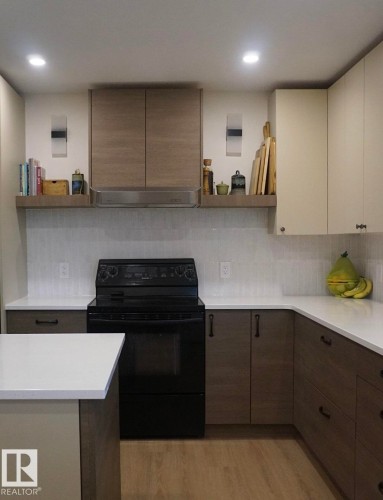 Modern kitchen featuring white countertops, a black electric range, a stainless steel range hood, and wood-finish flooring - 25 8930 99 Avenue, Fort Saskatchewan, AB 