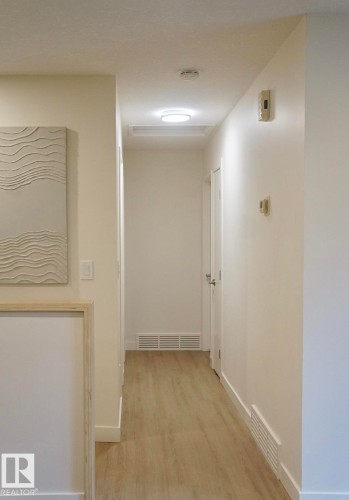 Hallway featuring wood-finish flooring, white baseboards, and a flush-mount ceiling light fixture - 25 8930 99 Avenue, Fort Saskatchewan, AB 