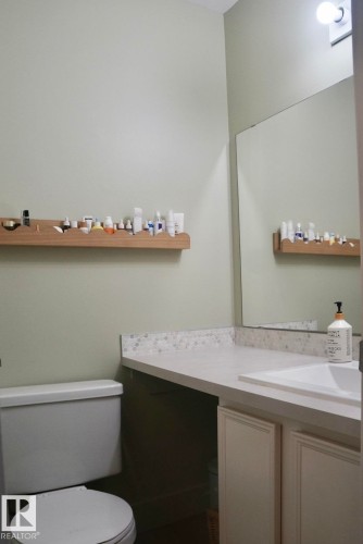 Bathroom featuring a white toilet, light-toned countertop with integrated sink, and full-width mirror - 25 8930 99 Avenue, Fort Saskatchewan, AB 