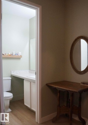 Powder room with a white toilet, white vanity with a rectangular sink, light-toned countertop, and wood-finish flooring - 25 8930 99 Avenue, Fort Saskatchewan, AB 