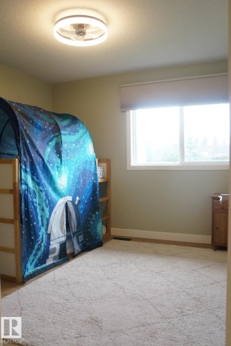 Carpeted room featuring a white window with a roller shade, light green walls, and a contemporary ceiling light fixture - 25 8930 99 Avenue, Fort Saskatchewan, AB 