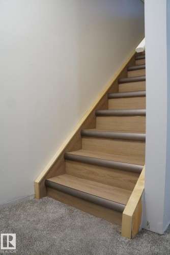 Staircase featuring wood-finish treads with dark trim, light wood stringers, and a carpeted landing - 25 8930 99 Avenue, Fort Saskatchewan, AB 