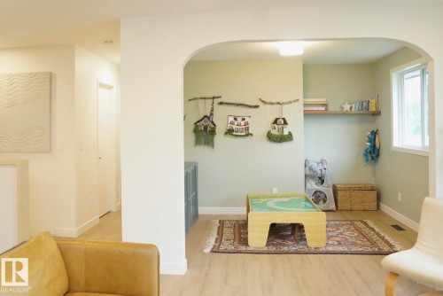 Arched entryway leading to a flexible space featuring wood-finish flooring, a window providing natural light, a built-in floating shelf, and neutral wall paint - 25 8930 99 Avenue, Fort Saskatchewan, AB 