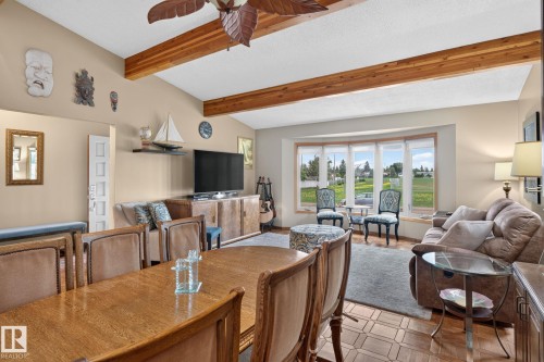 Vaulted ceilings with exposed wood beams define this open living space, featuring a bay window with a landscaped backdrop - 5808 Austin O'Brien Road, Edmonton, AB 