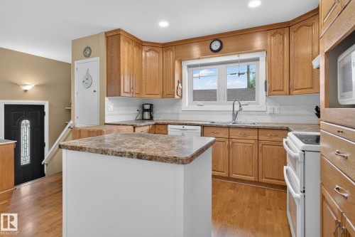 Kitchen featuring wood-finish cabinetry, a central island with a stone-finish countertop, and a double-basin sink - 5808 Austin O'Brien Road, Edmonton, AB 