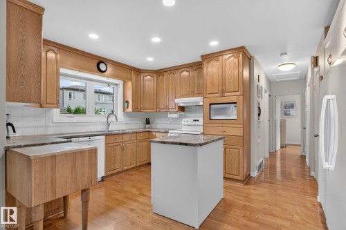 Kitchen featuring wood-finish cabinetry, granite-style countertops, an integrated microwave, recessed lighting, and wood-finish flooring - 5808 Austin O'Brien Road, Edmonton, AB 