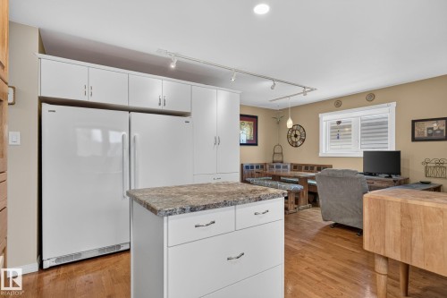Open-concept kitchen and living area featuring white cabinetry, a central island with a stone-finish countertop, wood-finish flooring, and recessed lighting - 5808 Austin O'Brien Road, Edmonton, AB 