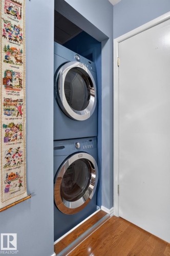 Main floor Dedicated laundry closet featuring a stacked washer and dryer in a blue finish, complemented by a wood-finish floor - 5808 Austin O'Brien Road, Edmonton, AB 