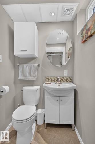 Basement Compact bathroom featuring a white wall-mounted cabinet, an oval mirror, and a vanity with a white ceramic sink - 5808 Austin O'Brien Road, Edmonton, AB 