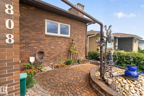 Brick exterior featuring a circular paver stone pathway, a raised garden bed with stone coping, and a window with white trim - 5808 Austin O'Brien Road, Edmonton, AB 