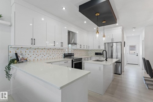 Modern kitchen featuring white cabinetry with black hardware, stainless steel appliances, and a patterned backsplash - 3606 42 Avenue, Beaumont, AB 