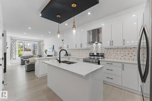Modern kitchen featuring glossy white cabinetry, stainless steel appliances, a white island with an undermount sink, and a patterned backsplash - 3606 42 Avenue, Beaumont, AB 